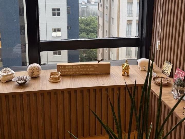 Bancada de madeira junto à janela do consultório, com objetos decorativos